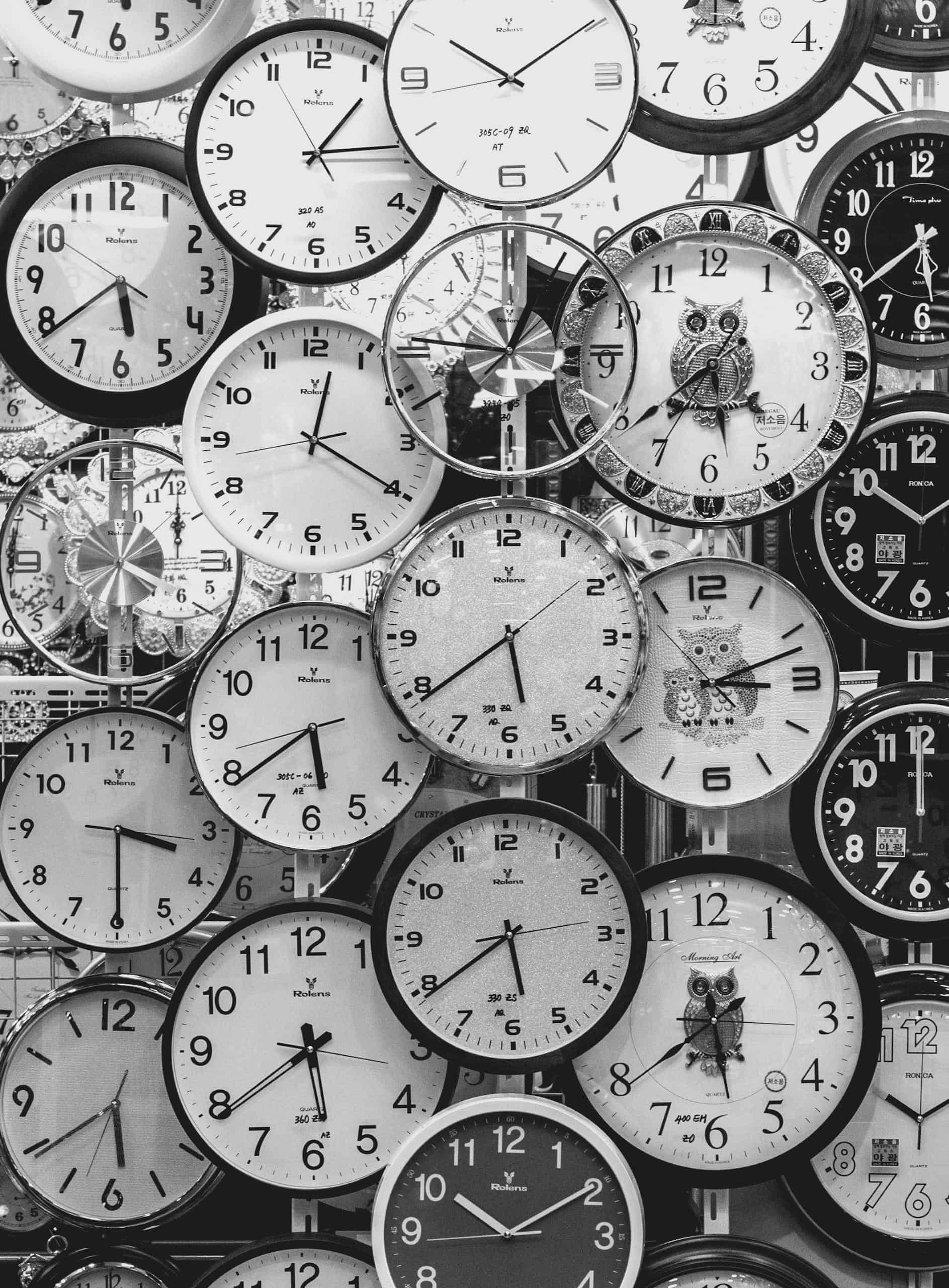 A black and white image displaying a diverse array of vintage wall clocks.